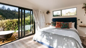 A bedroom with a large bed, a bathtub, and a sliding glass door to a garden. - River Haven Experience ultimate luxury in our cabin. (Whakamārama)