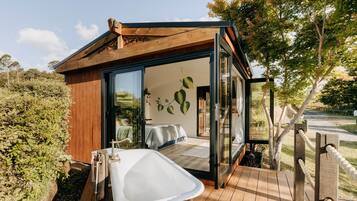 Eine moderne Holzhütte mit Glastür zu einem Schlafzimmer, einer Holzdiele und einer großen Badewanne.