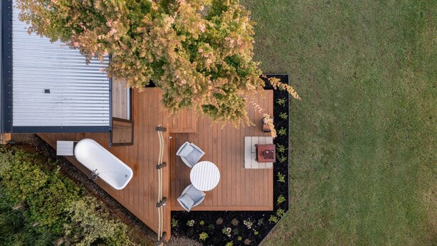 An aerial view of a deck with a hot tub, two chairs, a table, and a fire pit. - River Haven Experience ultimate luxury in our cabin. (Whakamārama)
