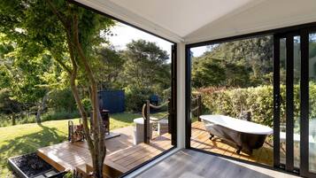 A modern bathroom with a freestanding bathtub, a wooden deck, and a glass door leading to a lush garden.