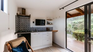 A modern kitchen with a large window, a flat-screen TV, and a view of a deck. - River Haven Experience ultimate luxury in our cabin. (Whakamārama)