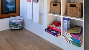 A room with a wooden floor, white walls, a framed picture, a shelf with books and a diffuser, and a rack with towels. - River Haven Experience ultimate luxury in our cabin. (Whakamārama)