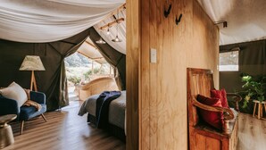 Alojamiento tipo tienda con una cama, una silla, una lámpara y un banco de madera.