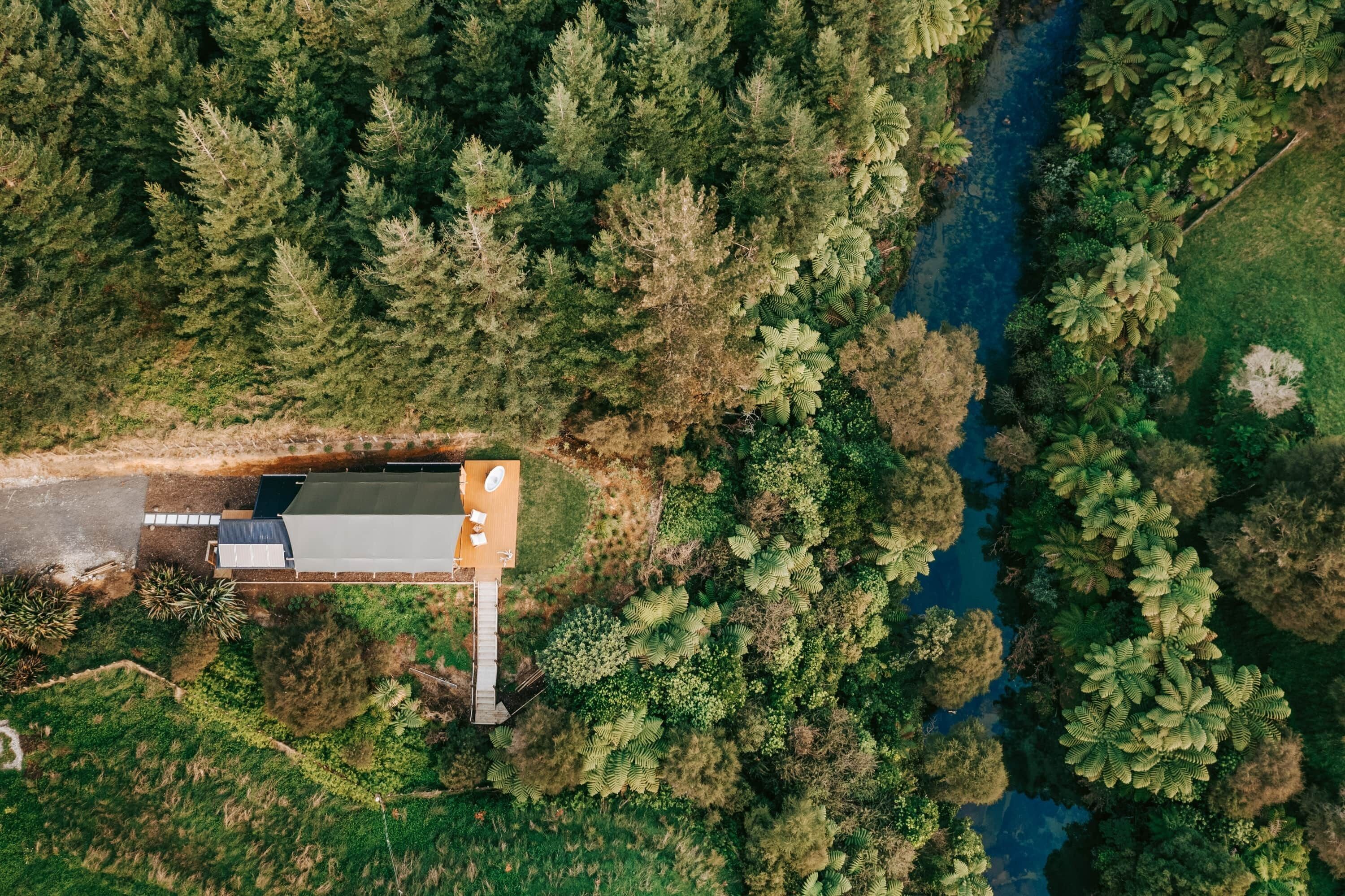 Et luftfoto af et hus med en terrasse, omgivet af tæt skov og en flod.