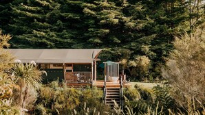 Una cabaña con terraza, rodeada de un bosque denso.