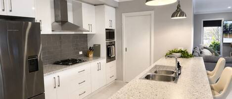 A modern kitchen with white cabinets, a stainless steel refrigerator, a granite countertop, and a built-in oven.