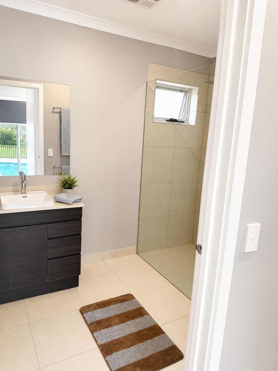 A bathroom with a shower, a sink, a mirror, and a towel rack.