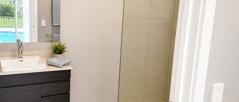 A bathroom with a shower, a sink, a mirror, and a towel rack.