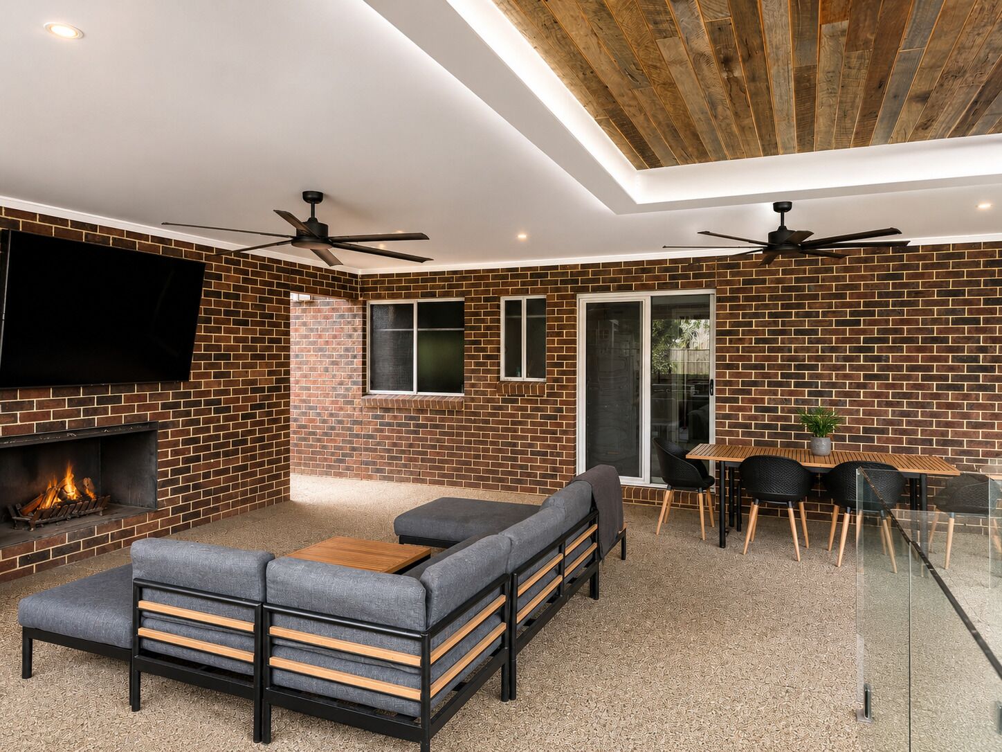 Un salon moderne avec un mur en briques, une cheminée, un canapé, une table à manger avec des chaises et des ventilateurs de plafond.