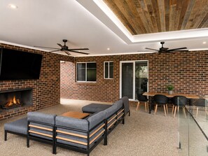 A modern living room with a brick wall, a fireplace, a sofa, a dining table with chairs, and ceiling fans. - Comfort on Clarke (Moama)