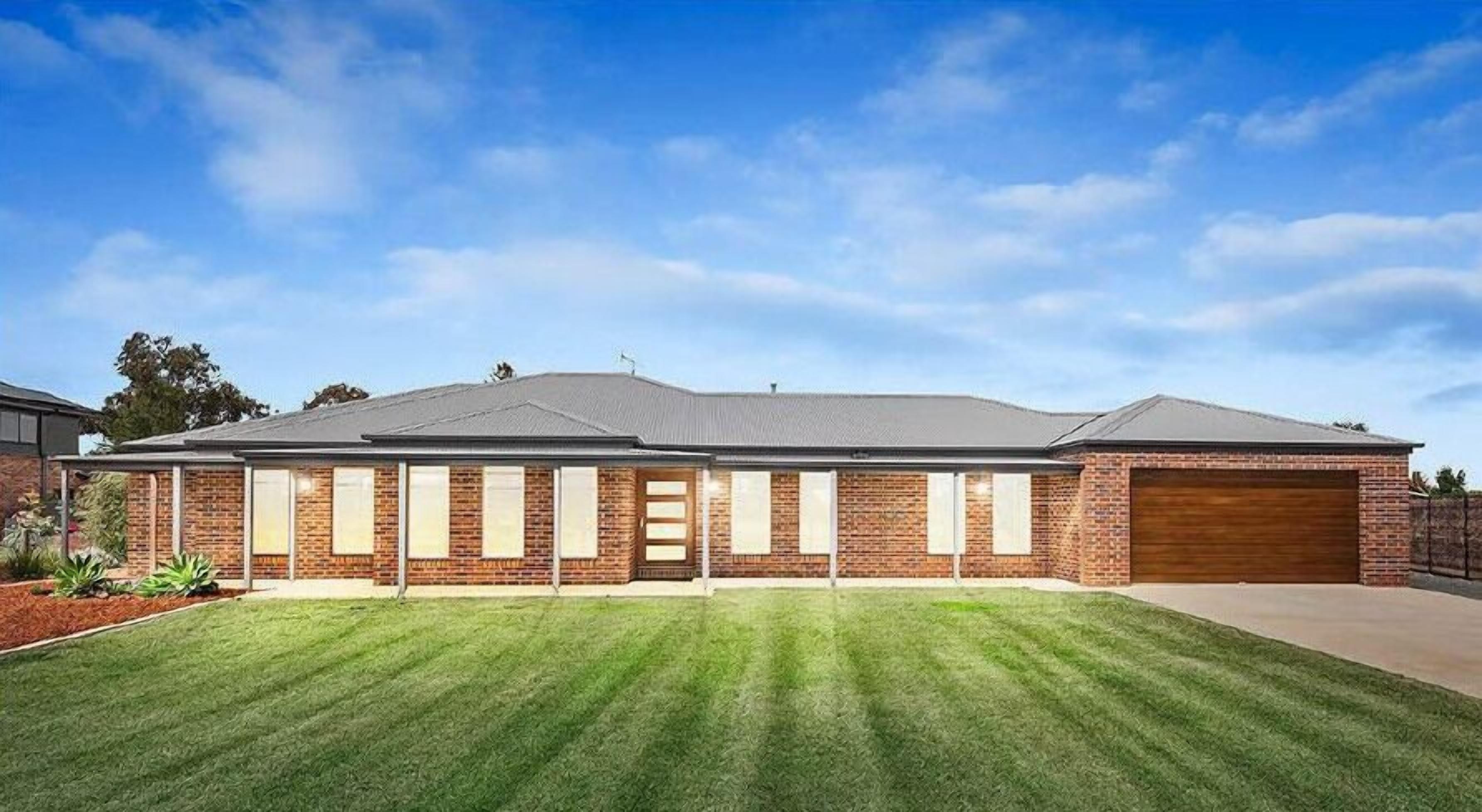 A two-story brick house with a front garage, a well-maintained lawn, and a clear sky.