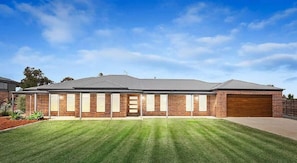A two-story brick house with a front garage, a well-maintained lawn, and a clear sky. - Comfort on Clarke (Moama)