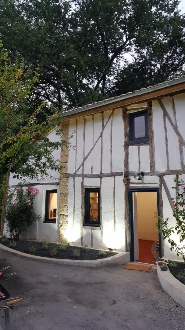 A half-timbered building with a door and windows, surrounded by trees and a paved area.