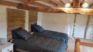 A bedroom with two beds, wooden beams, a white nightstand, and a hanging light fixture. - My Country House (EUGENIE LES BAINS)