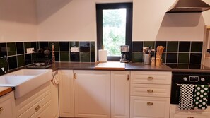 Una cocina con ventana, armarios blancos, una cafetera y un escurreplatos.