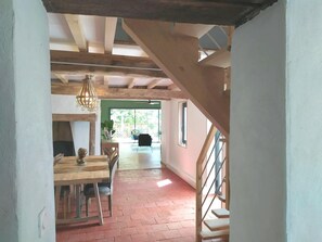 Un espacio interior con una escalera de madera, una zona de comedor con mesa y sillas, y vistas a un área exterior a través de una puerta de vidrio.