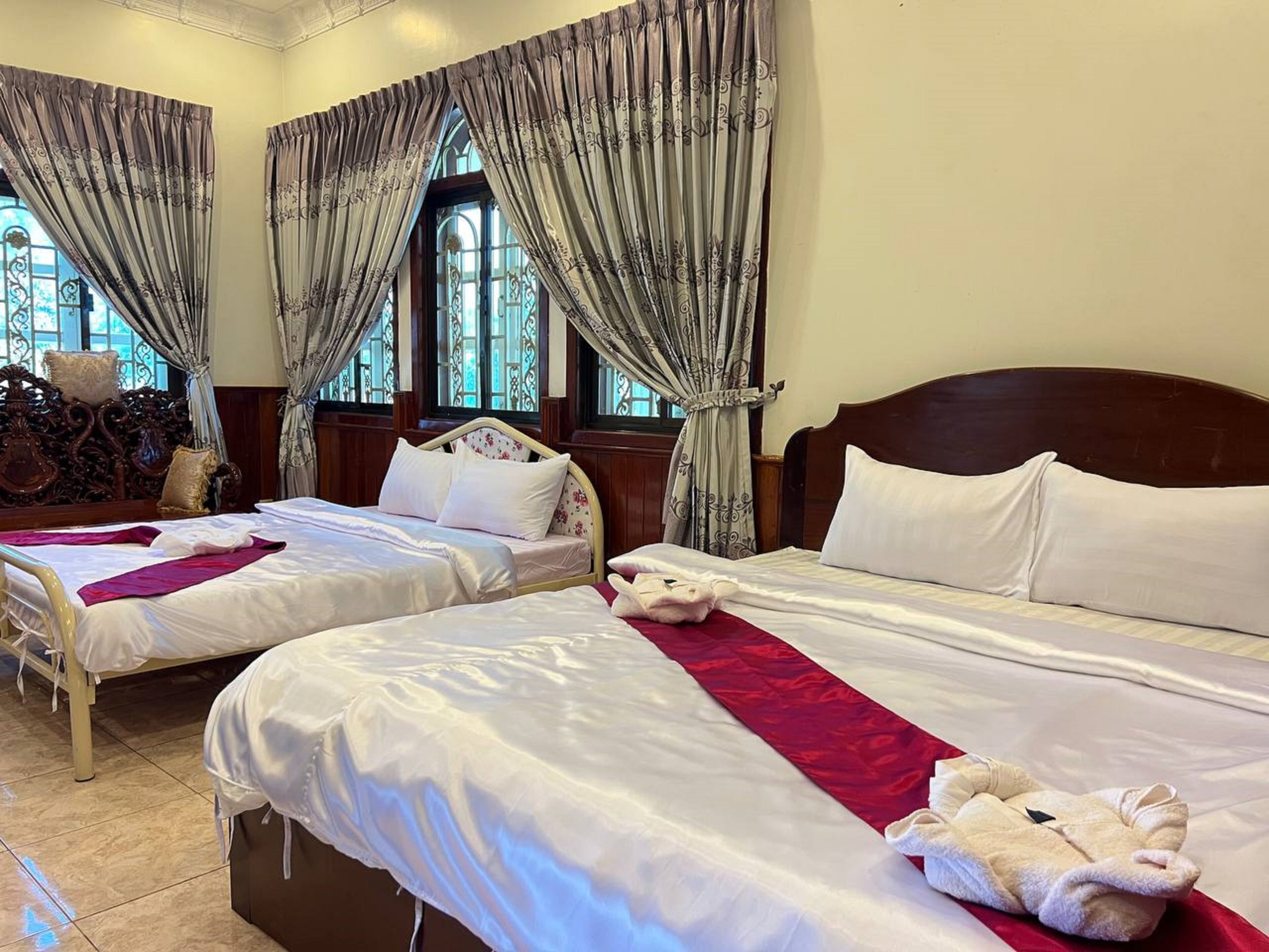 Habitación de hotel con dos camas, cabecera de madera, una alfombra roja y una ventana con cortinas.