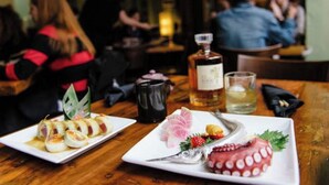 Un restaurante con una mesa de madera, platos de comida, una botella de licor y una copa.