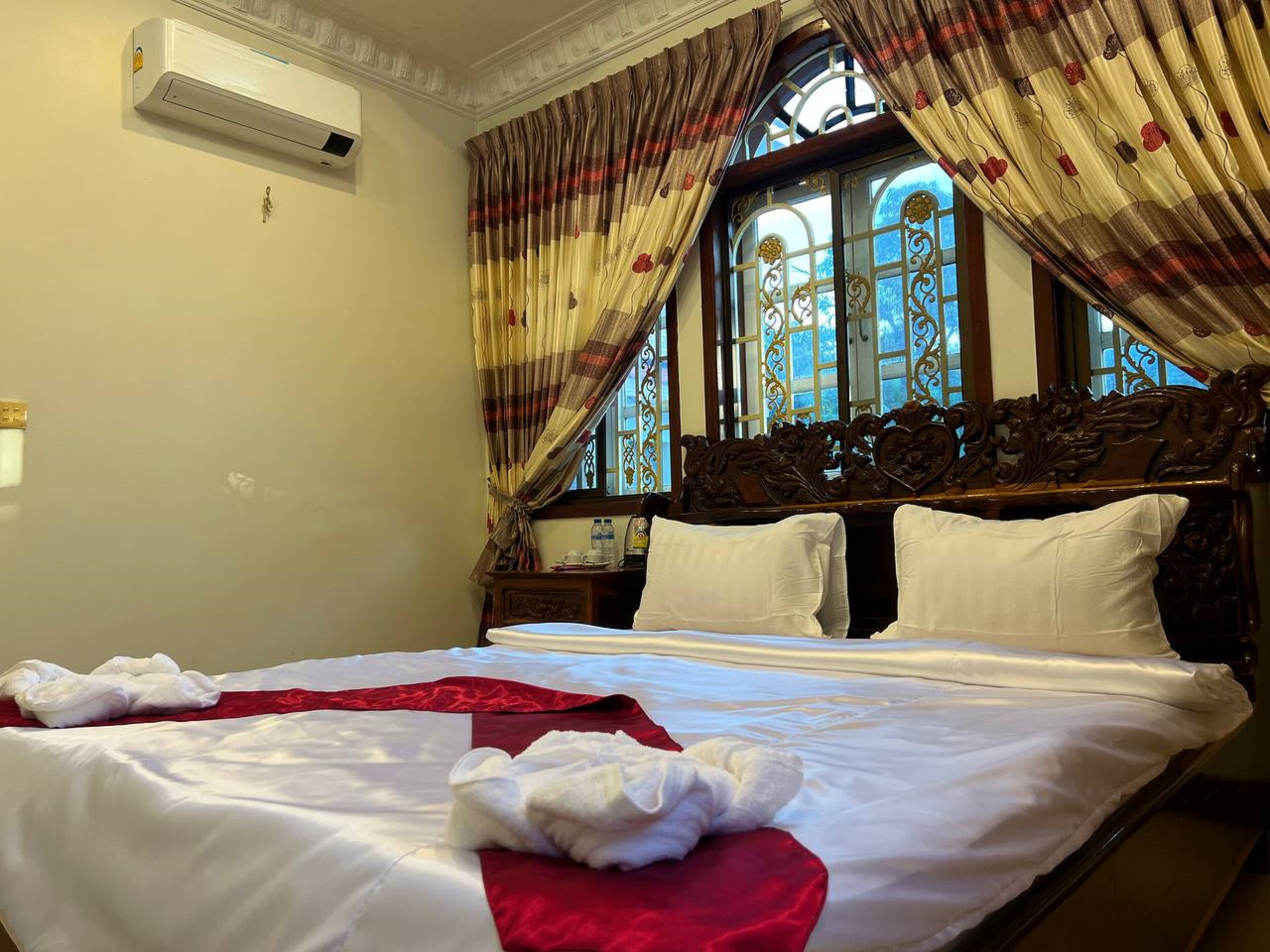 Habitación de hotel con una cama grande, una ventana con cortinas decorativas y un equipo de aire acondicionado instalado en la pared.