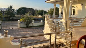 Un espacio al aire libre cubierto con una estructura de columnas blancas, barandilla metálica y un camino pavimentado.