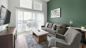 A modern living room with a sofa, armchair, coffee table, and a TV on a stand. - Landing | Beautiful 1BD (Nashville)