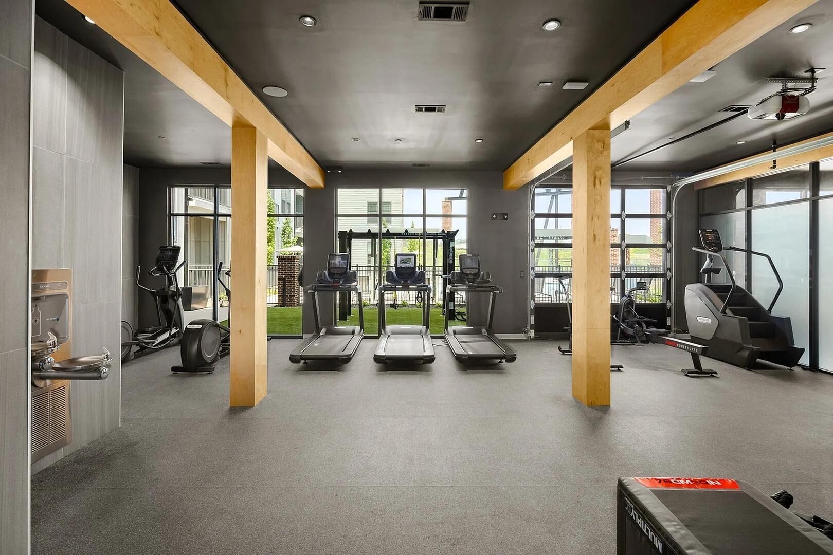 Ein Fitnessstudio mit Laufbändern, Crosstrainern und einem Ergometer, ausgestattet mit großen Fenstern und Holzbalken.