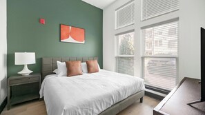A bedroom with a bed, a nightstand, a lamp, a painting, and a window with blinds. - Landing | Beautiful 1BD (Nashville)