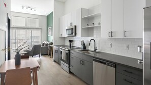 A modern kitchen with stainless steel appliances, a dining area with a table and chairs, and a view of the outdoors through large windows. - Landing | Beautiful 1BD (Nashville)