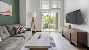 Ein modernes Wohnzimmer mit Sofa, Couchtisch, Fernseher und Blick durch Glastüren.