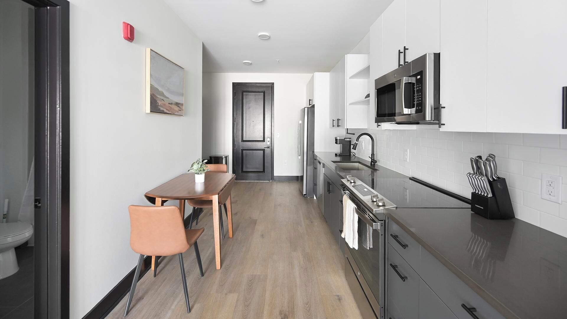A modern kitchen with a dining area, featuring stainless steel appliances, a wooden dining table, and a potted plant.