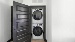 A laundry room with two stacked front-loading washing machines and a dark wooden door. - Landing | Beautiful 1BD (Nashville)