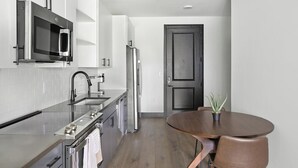 Une cuisine compacte équipée d’un four à micro-ondes, d’un four et d’un réfrigérateur. On y trouve une table à manger en bois avec des chaises et une plante en pot.
