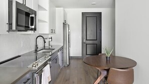 A compact kitchen with a microwave, oven, and refrigerator. There's a wooden dining table with chairs and a potted plant. - Landing | Beautiful 1BD (Nashville)