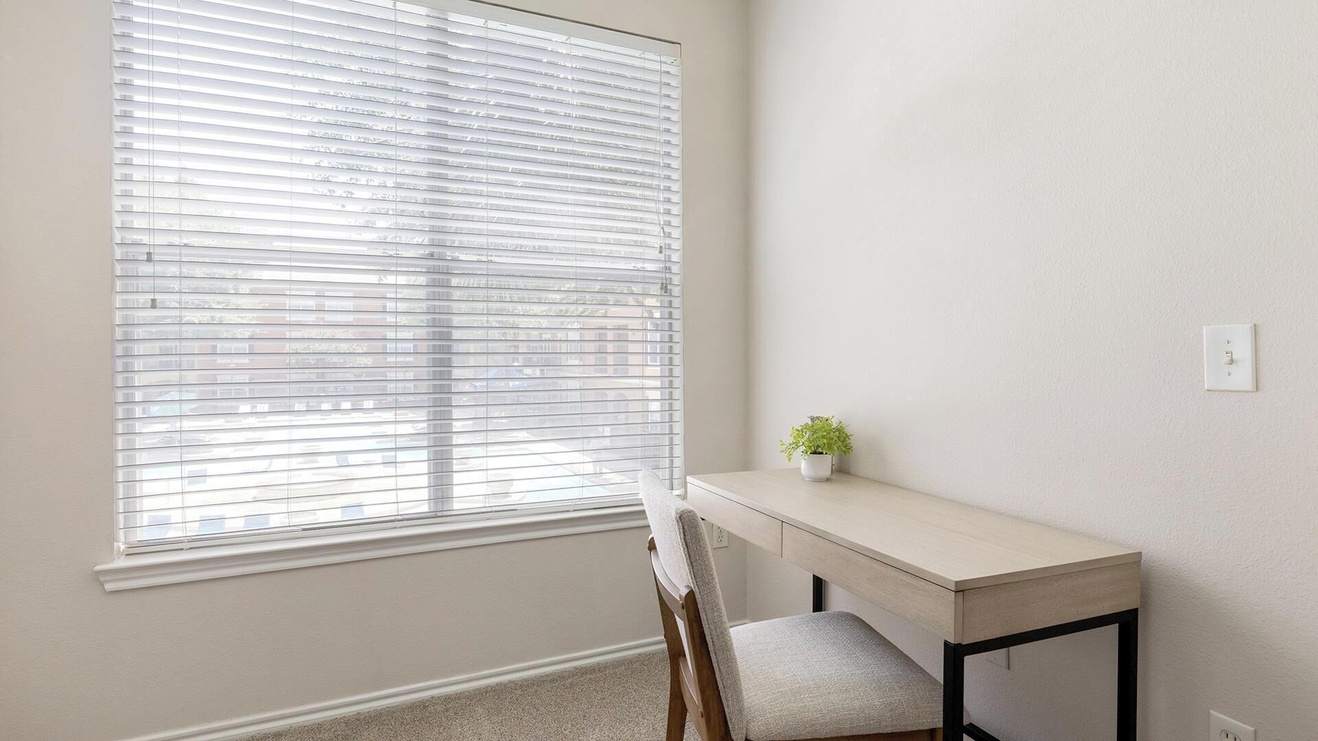 A room with a desk, chair, and a window with blinds.