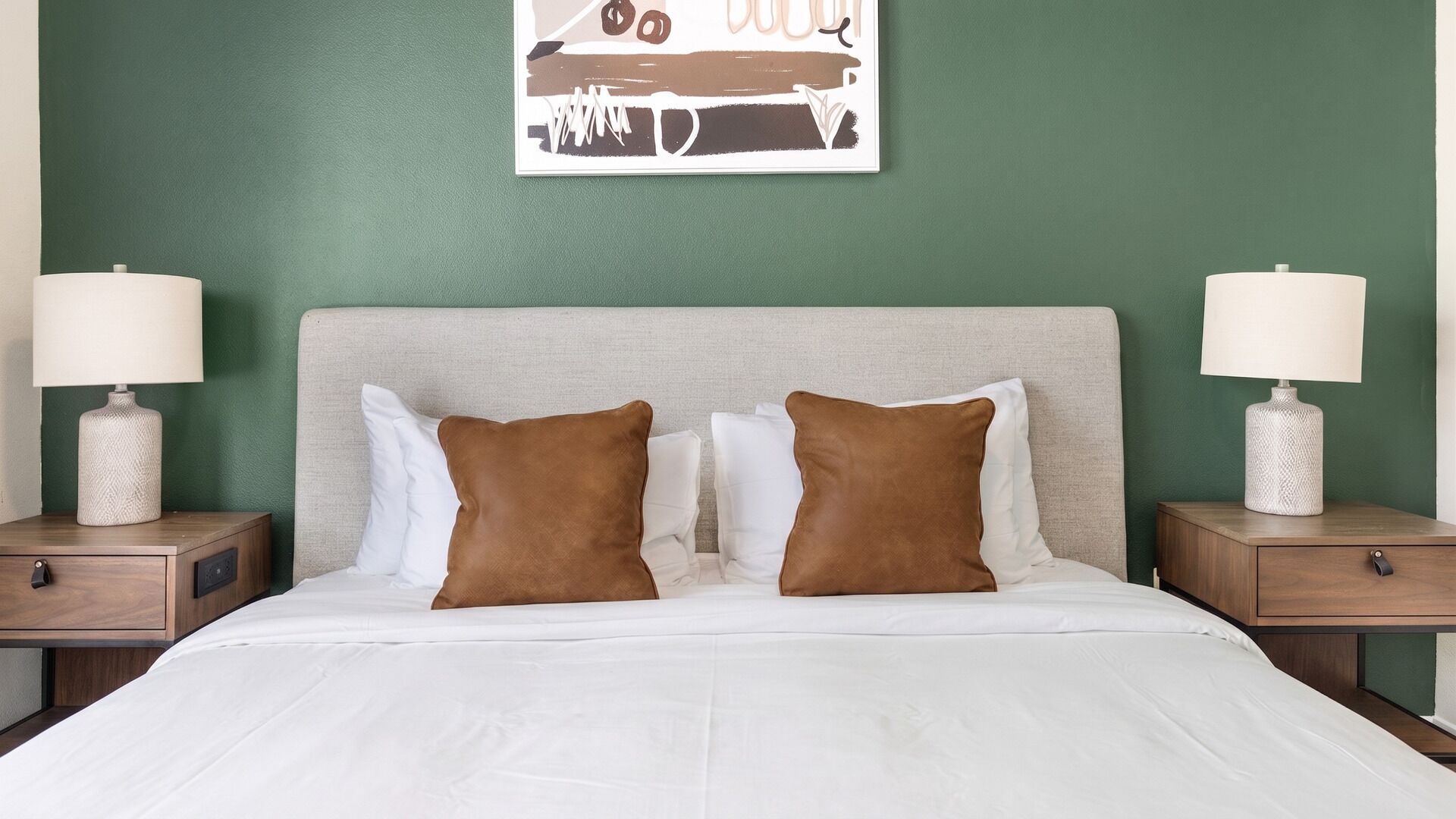 A hotel room with a bed, two nightstands, two lamps, and a wall art piece.