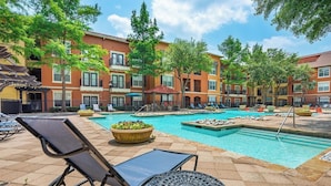 A pool area with lounge chairs, a small pool, and a building with multiple balconies. - Landing | Spectacular 1BD, Clubhouse (Irving)