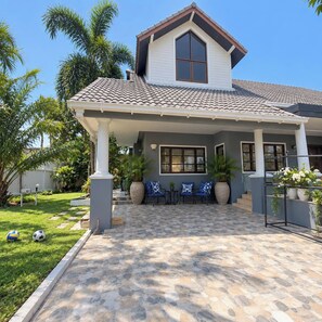 A house with a covered porch, stone flooring, and a garden with palm trees. - Luxury 3-bedroom villa with private pool in Pattaya (Muang Pattaya)