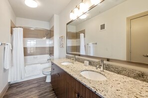 A modern bathroom with a shower, toilet, two sinks, a large mirror, and a vanity. - Landing | Modern 1BD, Clubhouse (Irving)