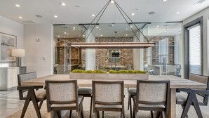 A modern dining area with a large rectangular table, four chairs, and a central planter with greenery. - Landing | Stunning 2BD, Gym, Courtyard (San Antonio)