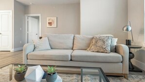 Een rustiek ogende woonkamer met een bank, een glazen salontafel en twee potplanten.