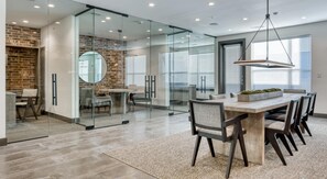 A modern interior with a glass-walled kitchen, a dining area with a large table and chairs, and a brick accent wall. - Landing | Spectacular 2BD, Gym, Courtyard (San Antonio)