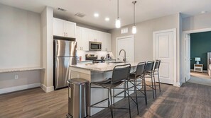 Een moderne keuken met roestvrijstalen apparatuur, een centraal eiland met barstoelen en uitzicht op een slaapkamer.