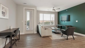 A living room with a sofa, a coffee table, and a TV mounted on a teal wall. - Landing | Stylish 2BD, Courtyard, Gym (San Antonio)