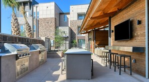 Eine Außenpatio mit Grillstation, Sitzgelegenheit und einem an einer Holzwand montierten Fernseher.