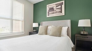 A bedroom with a bed, two bedside tables, a window with blinds, and a framed picture on the wall. - Landing | Incredible 2BD, Courtyard, Gym (San Antonio)