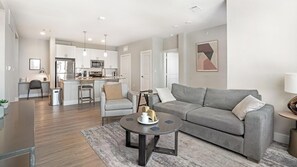 Ein modernes Wohnzimmer mit einem grauen Sofa, einem Couchtisch und einer Küche im Hintergrund.