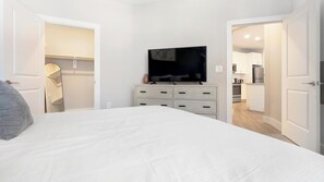 Une chambre à coucher comprenant un lit, une télévision, une armoire et une porte ouverte donnant sur une cuisine.