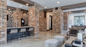 A modern kitchen with a brick accent wall, a bar area with stools, and a seating area with ottomans. - Landing | Incredible 1BD, Gym, Courtyard (San Antonio)