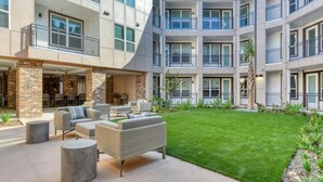 Un edificio de varios pisos con un patio que cuenta con mesas al aire libre y un césped bien cuidado.