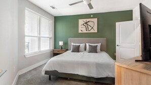 Un dormitorio con cama, mesita de noche, lámpara, ventilador de techo y un cuadro en la pared.